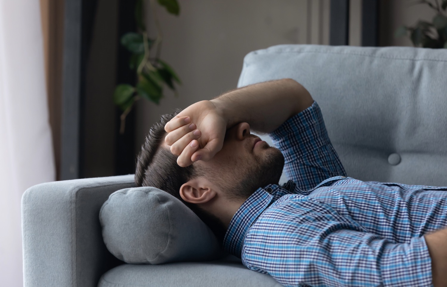 Homme souffrant d'une migraine, allongé avec le bras sur les yeux
